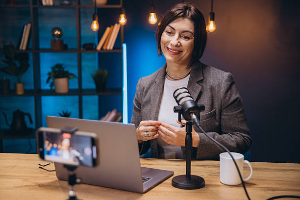 istock Happy female podcaster speaking into microphone and recording audio podcast at home studio using laptop and smartphone 2243935302