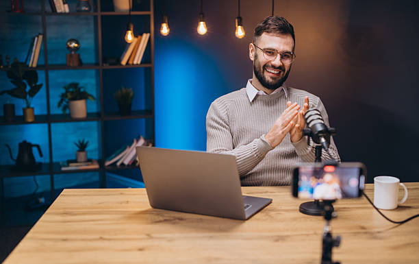 istock Happy podcaster speaking and clapping hands during a live podcast recording in his studio with laptop and smartphone 2243935421