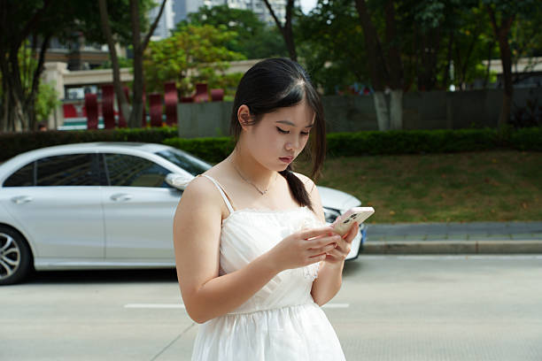 A young woman in a white dress is using a smartphone.