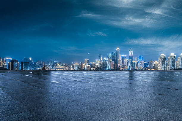 Empty square floor with modern city skyline and illuminated commercial buildings at night.