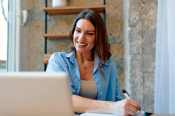 istock Woman working remotely online from home smiling and writing notes 2243945715