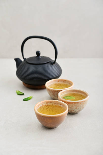 istock Black cast iron teapot and three ceramic cups of green tea 2243948474