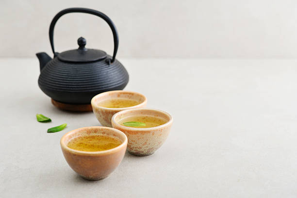 istock Black cast iron teapot and three ceramic cups of green tea 2243948485