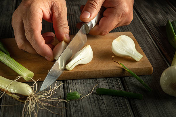 istock Hands expertly slice fresh green onions on a wooden board. The setting features a rustic kitchen with natural light illuminating the scene, capturing a moment of cooking preparation 2243960501