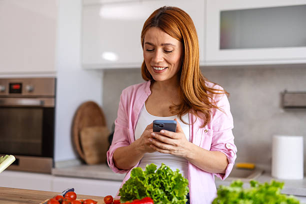 istock A woman in a modern kitchen prepares dinner while taking food photo, capturing a fun and joyful moment. She is multitasking, cooking a delicious homemade meal while enjoying the process. 2243962010