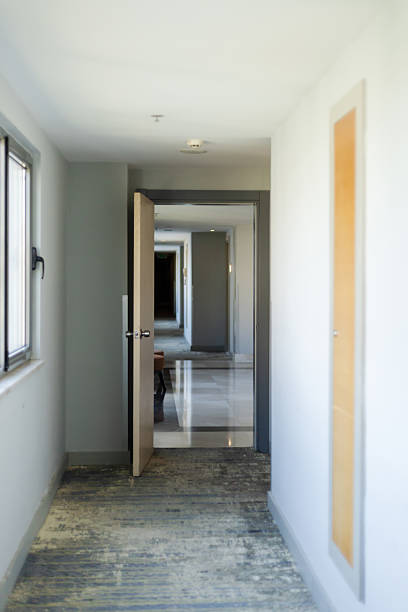 A long hallway shows several open doors on both sides. Natural light fills the space, highlighting the clean lines and modern design. The floor appears sleek and polished.