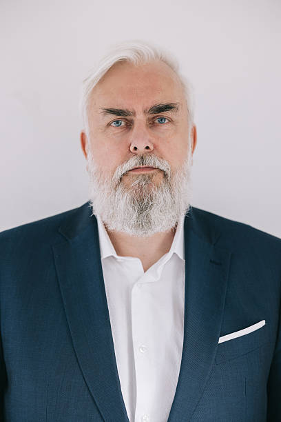 A confident and professional-looking mature man in a suit and white shirt poses for a formal portrait, set against a light and minimalistic background, conveying professionalism, wisdom, and experience.