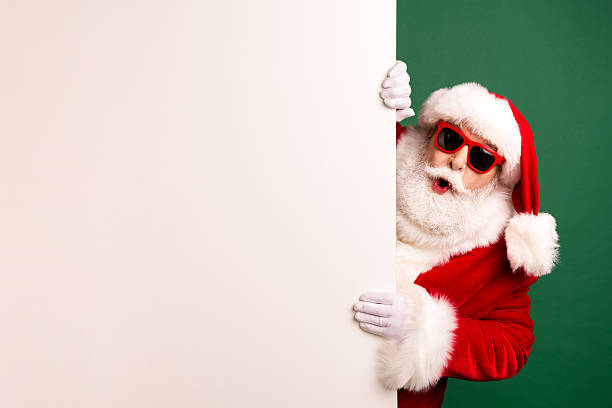 istock Santa peeks from a white panel wearing a red suit a hat and sunglass against a green backdrop in a playful holiday scene 2243964440