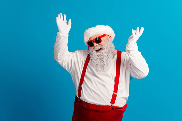 istock Santa with red suspenders dancing and smiling in a bright blue studio background during Christmas wearing a hat gloves and red pants for festive mood and holiday sales 2243965337