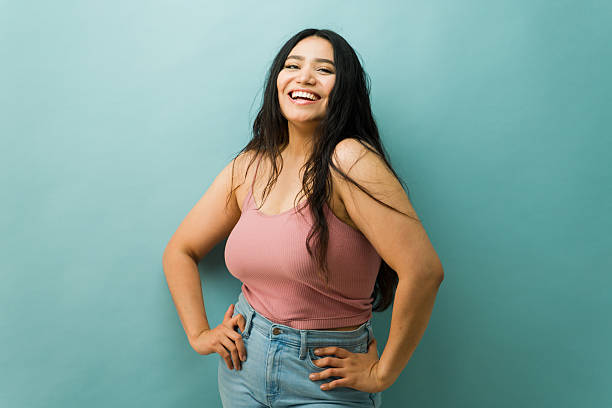 Woman laughing, posing in a studio with a light blue background. She is showing a happy and cheerful mood