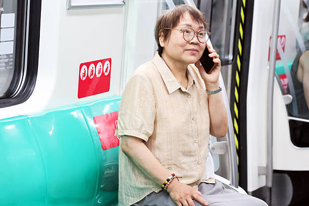 An elderly Asian woman using her mobile phone on the subway.