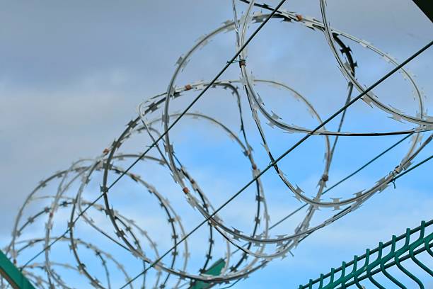 istock Barbed razor wire on a high-security building. Barbed wire and hard wire fence. Concepts for jails, army facilities, nuclear power plants, and defense against illegal migration. 2243973291