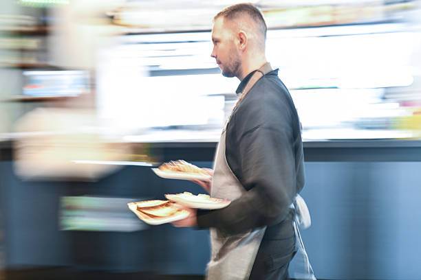 Busy Chef In Apron Carrying Plates Through Blurred Kitchen At Breakfast Bar Early Morning