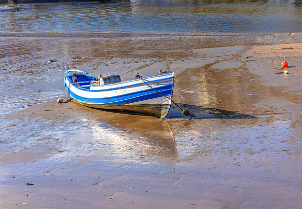 Whitby, UK. October 10, 2025. A boat is moored aground in a harbour with a barrel in the centre of the boat. The boat is reflected in the muddy water.