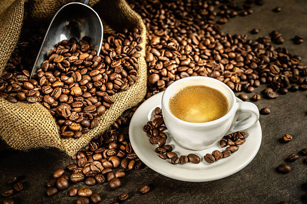 Roasted coffee beans spilling from a burlap bag next to a rich cup of espresso