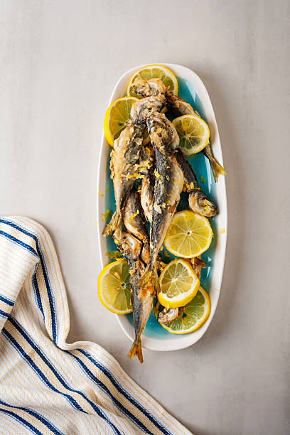 Cooked oven istavrit. Fried horse mackerel fish istavrit. Fried horse mackerel istavrit fish on a plate with lemon on the gray background.