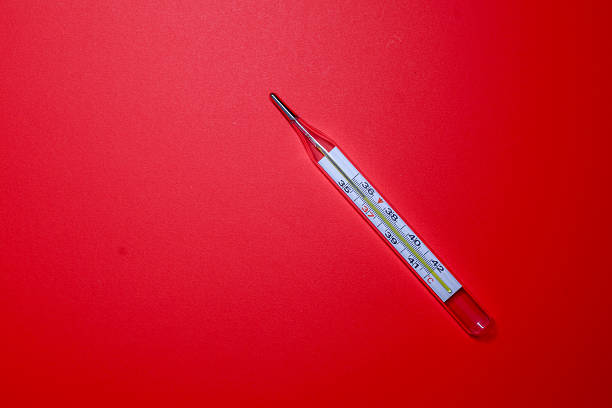 A classic glass thermometer for measuring body temperature is positioned on a saturated red background. This essential item, associated with first aid and monitoring, serves as a powerful visual element.