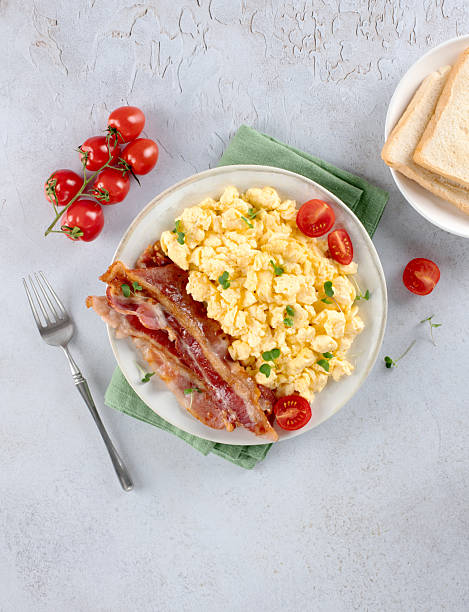 istock Scrambled eggs with crispy bacon and tomatoes on a white background. Top view. 2243990950