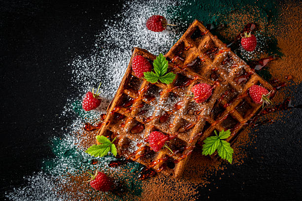 istock Fresh baked chocolate Belgian waffles with red raspberries and jam on black plate for breakfast, closeup, top view. Culinary, cooking, bakery concept. Food recipe background. Sweet waffles with berry 2243990993
