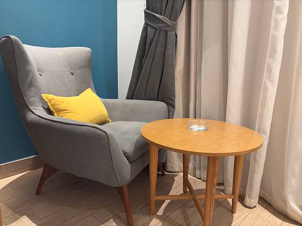 Stylish home interior, modern cozy corner with chair and table, grey modern chair, wood table, modern furniture, hotel room interior.