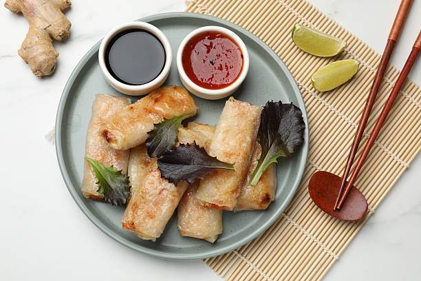istock Tasty fried spring rolls, lettuce, sauces and other products on white marble table, flat lay 2243994271