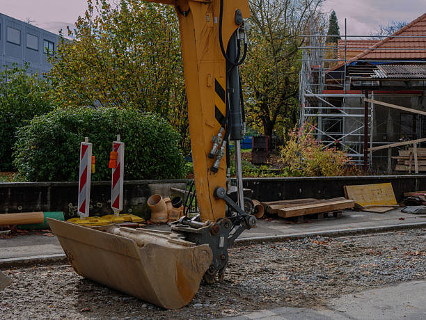 Excavator bucket on urban road construction site with red and white barriers, digging equipment and scaffolding in background. Pro photo. High quality