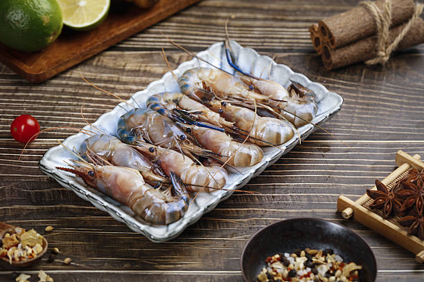 Fresh Raw Prawns Shrimp Seafood in Tray with Lime and Spices on Wooden Table Kitchen Preparation Fresh raw prawns and shrimp in white tray on rustic wooden table with lime, spices and cooking ingredients for seafood preparation rochester restaurants stock pictures, royalty-free photos & images