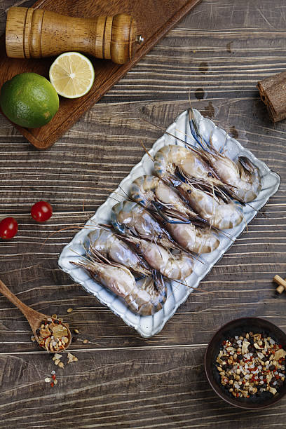 Fresh Raw Prawns with Lime and Spices on Wooden Background - Seafood Cooking Ingredients Fresh raw prawns in white tray with lime, cherry tomatoes and spices on rustic wooden background, ready for cooking seafood dish rochester restaurants stock pictures, royalty-free photos & images
