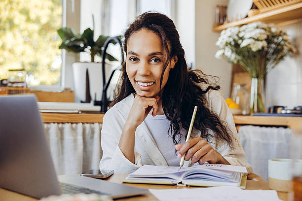 istock Smiling writer, African American woman taking notes, using laptop, working at home looking at camera 2244013029