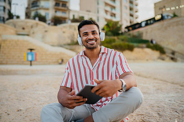 istock Man sitting with tablet and headphones on the beach 2244022091