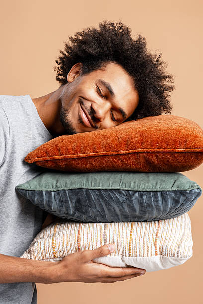 istock African American man holding pillows sleeping isolated on beige background. Advertisement concept 2244024095