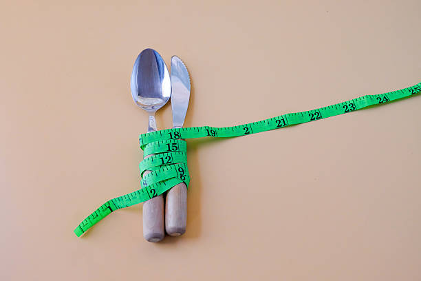 Green Measuring tape on a spoon and fork on color background.