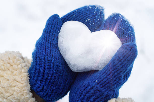 A heart made of snow is held by hands in blue mittens