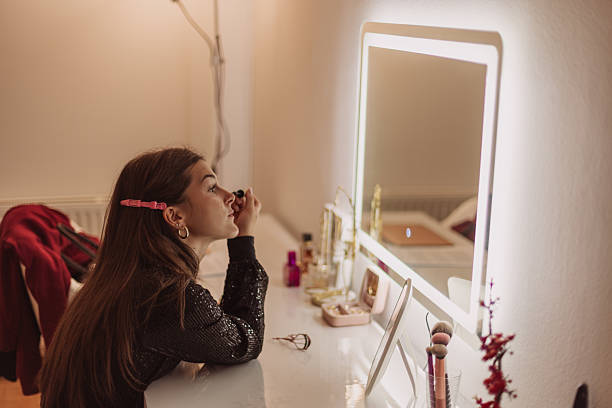 istock Young Woman Applying Makeup At Illuminated Vanity Mirror In Cozy Bedroom Setting 2244028387