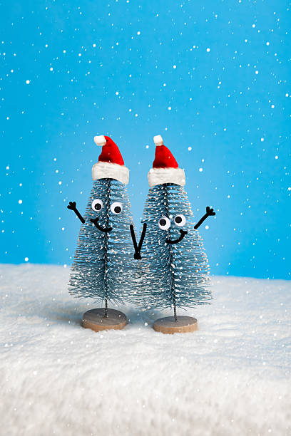 A pair of ornamental Christmas trees with googly eyes and stick figure arms holding hands in love in the snow.