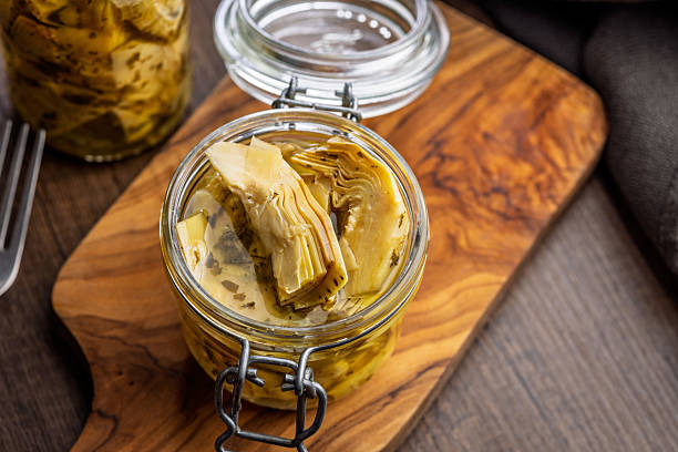 Pickled artichoke in jar on a wooden table.