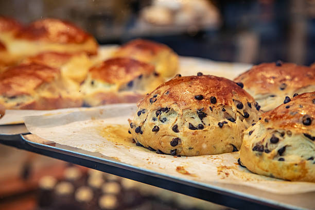 Close-up view of freshly baked Belgian Cramique bread filled with chocolate chips displayed on a baking tray inside a local bakery in Bruges, Belgium. The golden brown crust and soft texture highlight the artisanal craftsmanship of this traditional sweet brioche, a popular treat in Belgian cafes and patisseries enjoyed with coffee or hot chocolate.