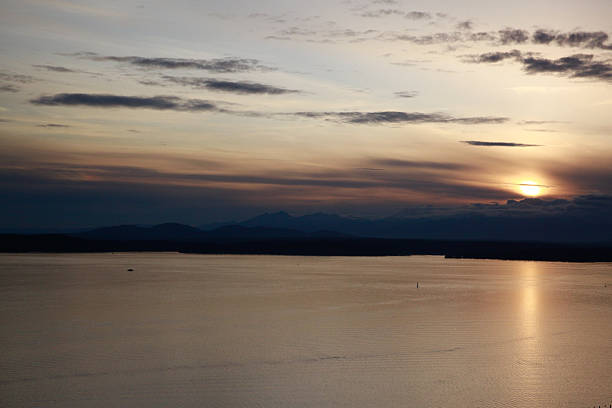 Golden sunlight reflects on the water as the sun sets behind distant mountains. The sky features hues of gold and blue, creating a peaceful atmosphere during twilight.