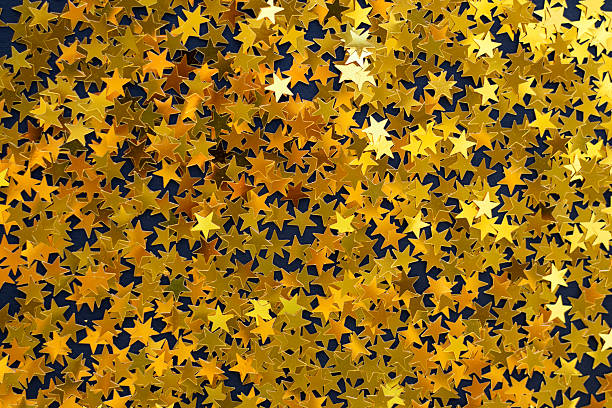 Golden star confetti scattered on yellow background for festive celebration and sparkle themes.