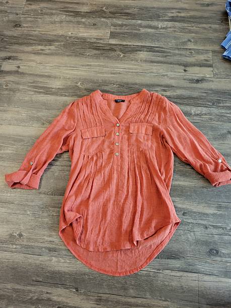 An orange shirt is currently laying flat on a wooden floor
