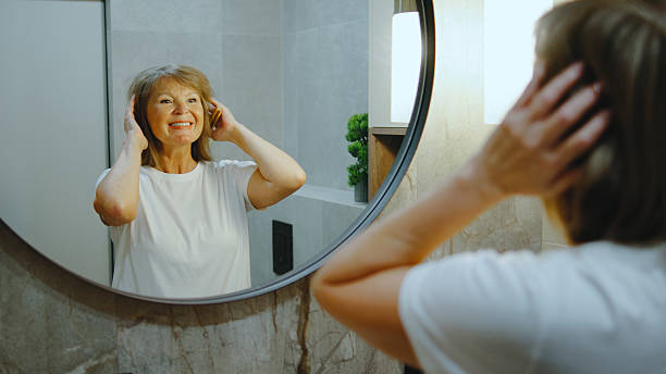 istock Elderly woman smiling in mirror while adjusting hair in bright bathroom during morning routine 2244042620
