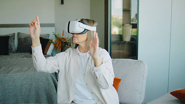 istock Elderly woman experiences virtual reality in a modern living room, engaging with immersive content while seated on a cozy sofa 2244044815