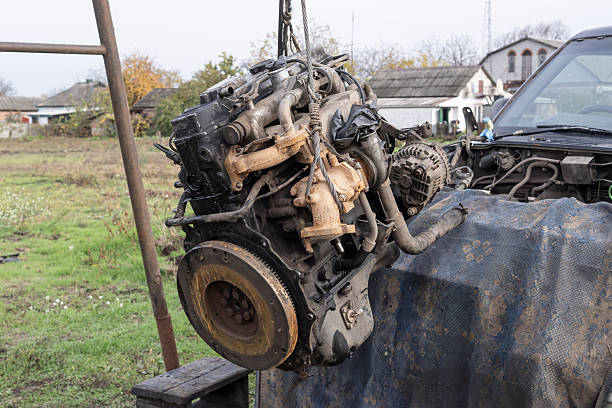 Old engine hanging on a hoist in a workshop yard. Concept of vehicle repair, maintenance, mechanic work, and engineering details in industrial setting.
