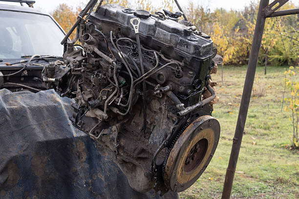 Old engine hanging on a hoist in a workshop yard. Concept of vehicle repair, maintenance, mechanic work, and engineering details in industrial setting.