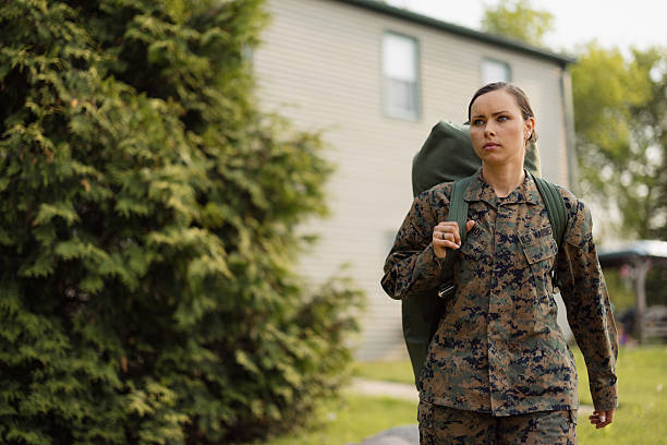 Serious woman Marine veteran wearing camouflage uniform walking outdoors with a duffel bag on her shoulder