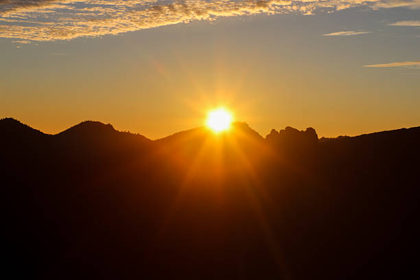Sun setting behind the silhouetted peaks of Roques de Garcia in Teide National Park, highlighting the warm sky