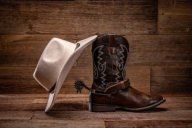 Traditional cowboy boot with spur and white hat, placed profile on a rustic retro wooden background. Classic western footwear symbolizing rodeo, ranch life, country music, and cowboy culture. Perfect for themes of Americana, rustic lifestyle, vintage western style, and authentic cowboy gear. The composition includes copy space for text, making it ideal for advertising, posters, or editorial use related to western heritage, rodeo events, ranching, farming, country living, or rustic outdoor lifestyles.