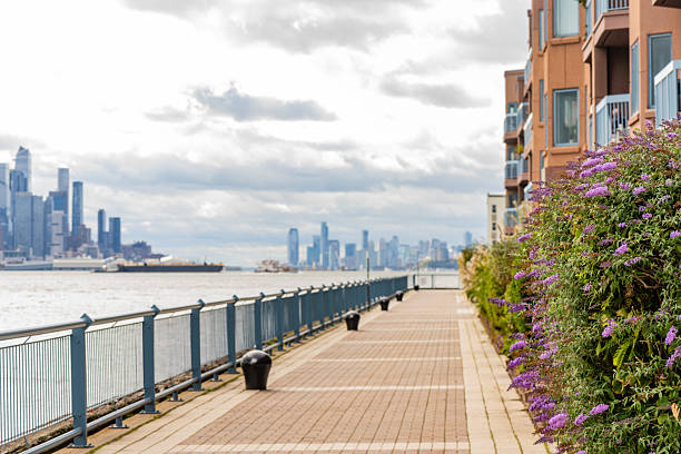 This is a photograph of the walking path along the Hudson River in  Edgewater, New Jersey on an overcast, autumn day with the Manhattan city skyline visible in the background.