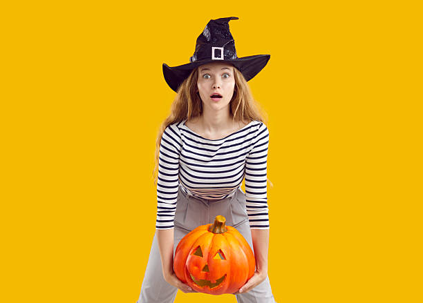 istock Witch with Halloween pumpkin looking at camera with funny scared surprised face expression 2244058036