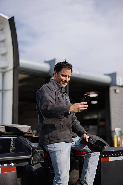 istock Truck driver using smartphone app sitting on truck trailer 2244059194